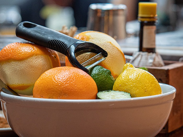 White porcelain bowl filled with oranges, lemons, limes and a black peeler